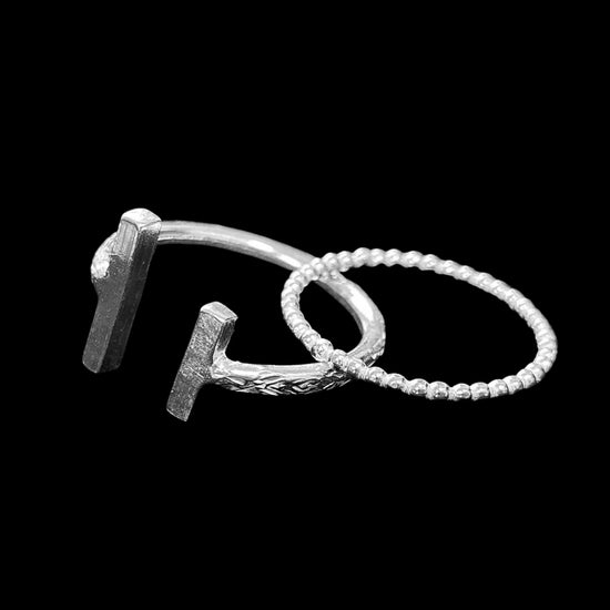 Shows 2 rings laying over each over. A silver small ball ring and a larger patterned ring with rectangle bars at the ends with a gap.