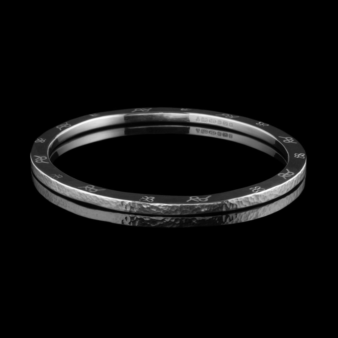 A thick textured sterling silver bangle with personalised symbols engraved onto the sides. A hallmarked bespoke jewellery commission by NI Silver.
