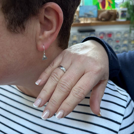 You can make your own jewellery during our workshop experiences, this image shows a lady with her hand over the shoulder of another lady.  There is a new silver ring on the hand and close by in the ear of the other lady is a triangular small earring.