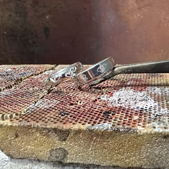 2 Handmade rings from people on our workshops, that have been stamped with their initials and love hearts. Photographed placed on a heat block in the NI Silver workshop.
