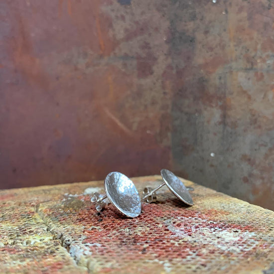 2 small silver circle earrings that have been domed and textured. Handmade jewellery by NI Silver.