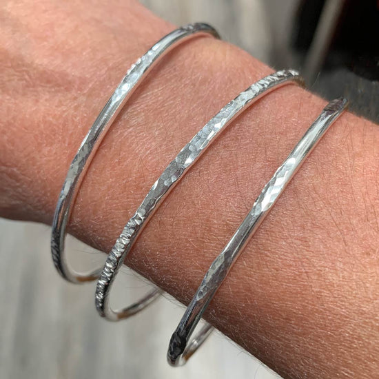 Shown on a lady's arm these 3 silver handmade bangles have differing hammered textures on them.