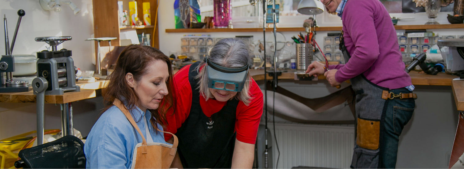 Ruth our goldsmith leans in to explain a technique to a seated lady in our workshop.