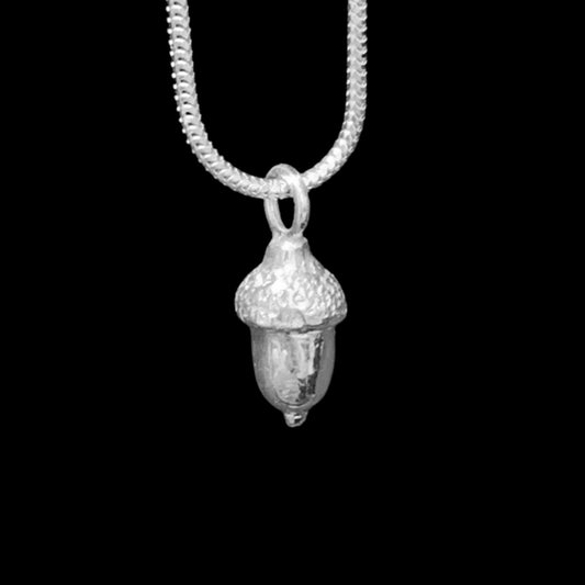 A close up of the NI Silver Acorn necklace hanging on a silver snake chain.