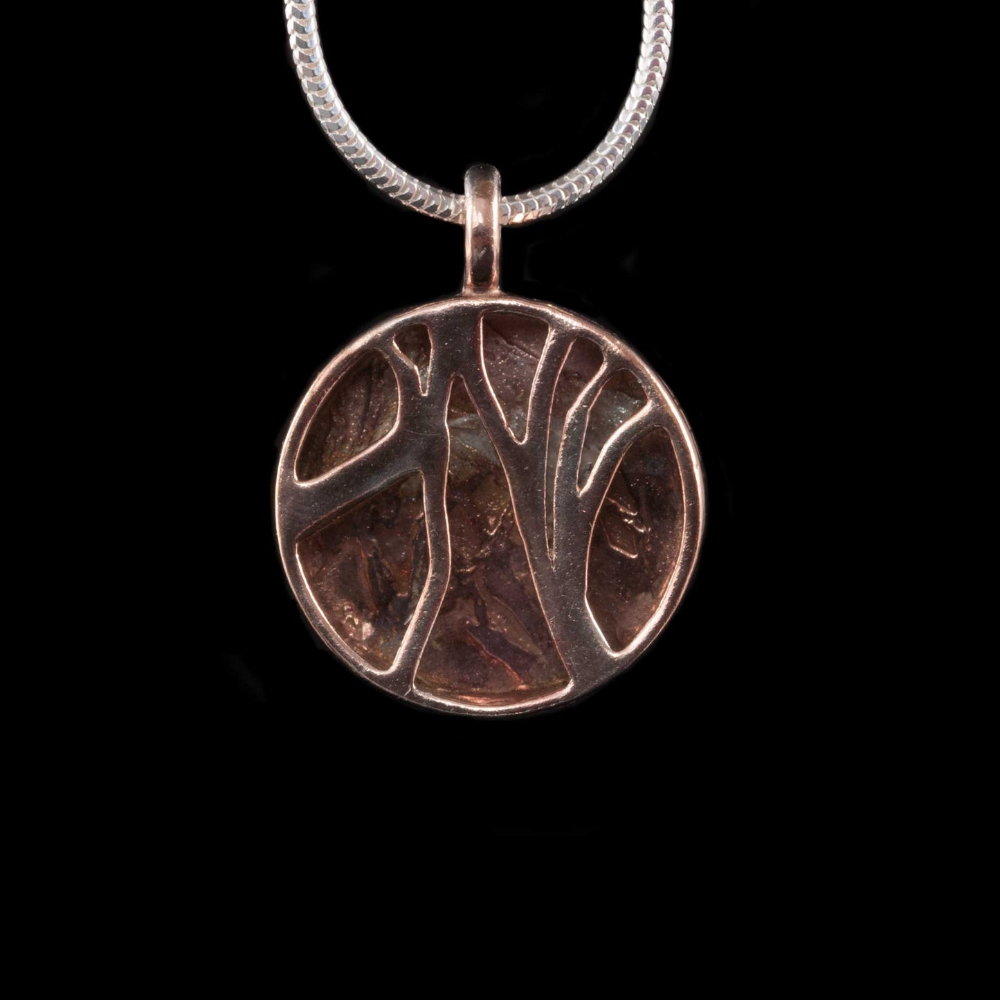 This is a close up of the front of NI Silver Jewellery's Dark Hedges Rose Gold Plated silver necklace. The front is the image of 2 trees lining the road to Gracehill House at the Dark Hedges.