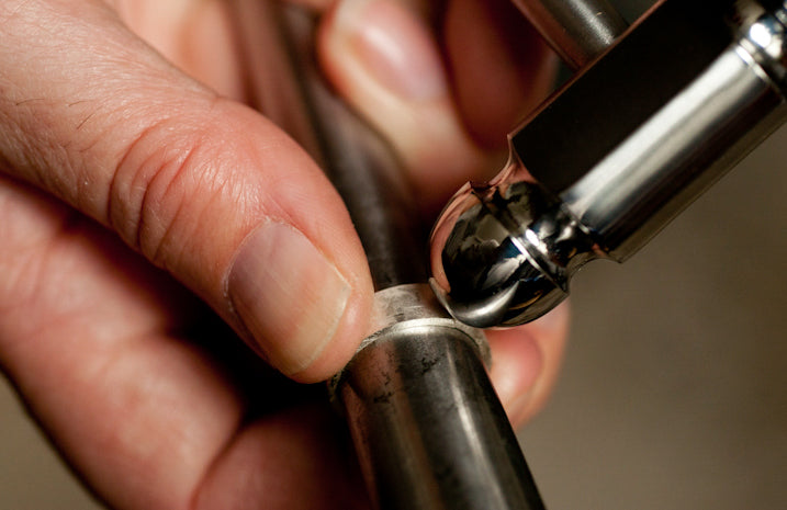 A ring being held in the hand against a mandrel as a jewellery making hammer is placed against it.