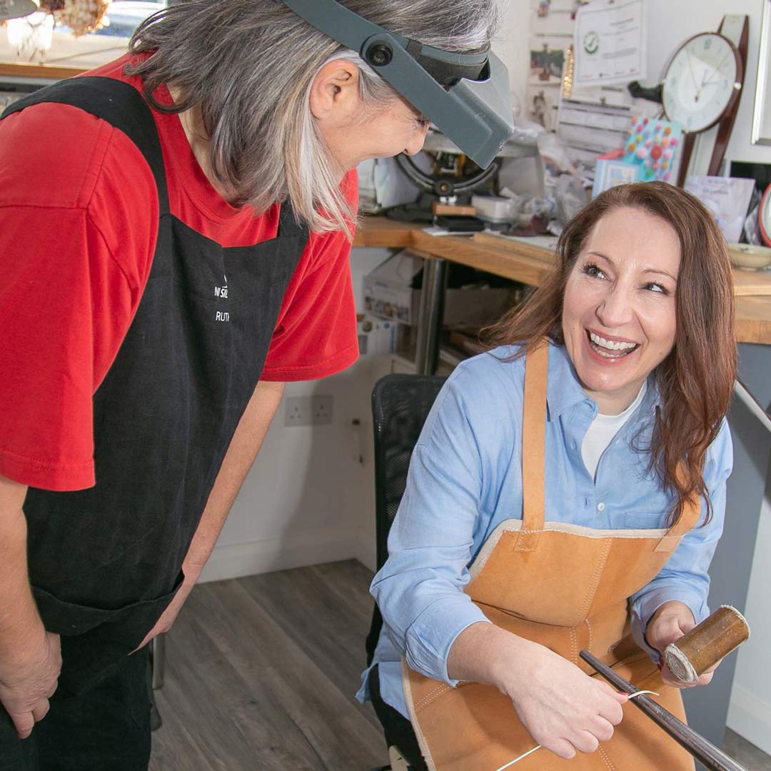 Ruth our jewellery maker laughing with a lady as she hammers a piece of silver during one of our NI Silver jewellery experiences.